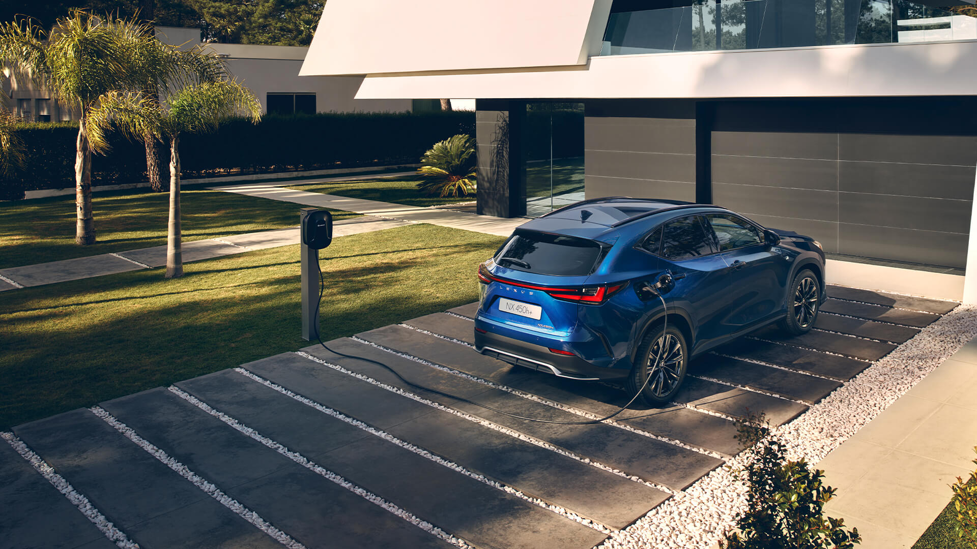 A Lexus NX 450h+ plugged into a charging station outside a home